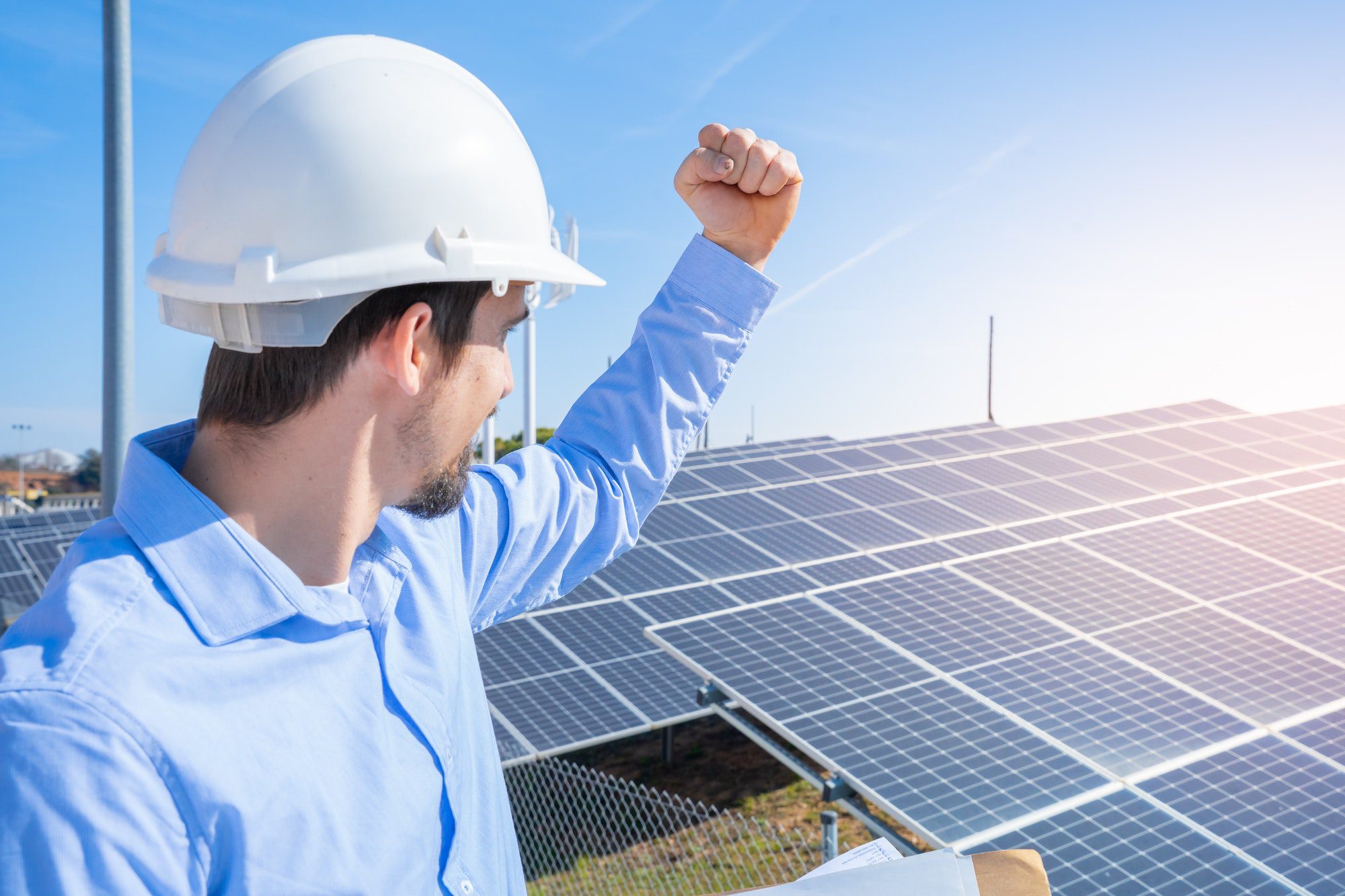 Happy engineer in protective helmet on a solar power plant celebrating success.