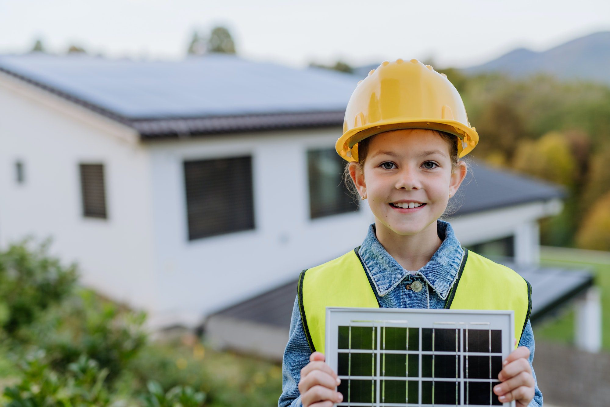 Little girl with protective helmet and reflective vest holding photovoltaics solar panel