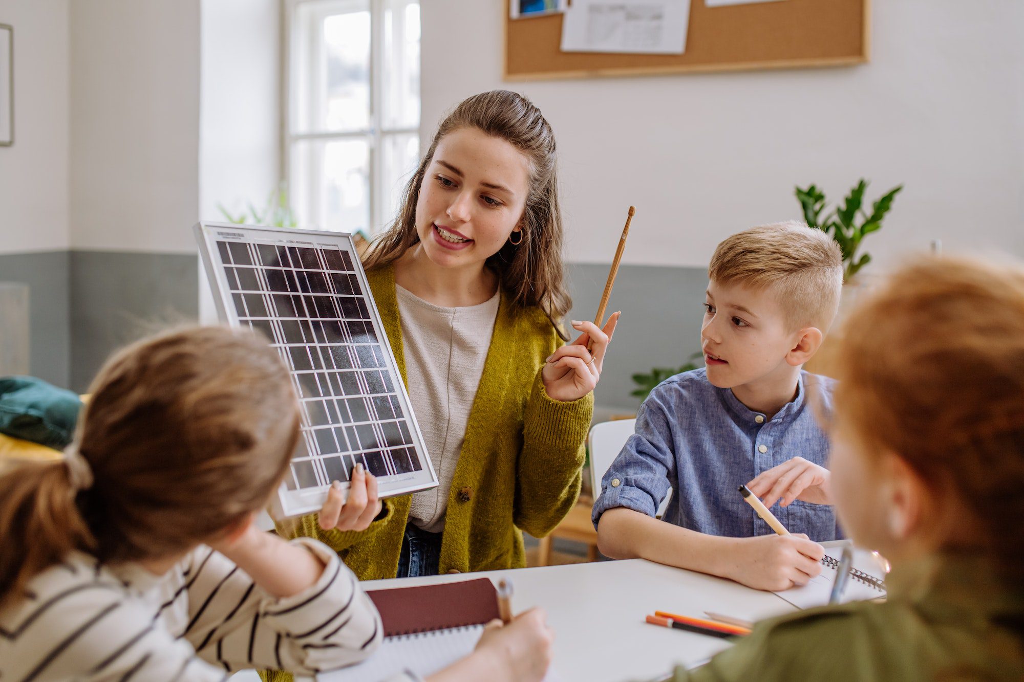 Young teacher with solar panel learning pupils about solar energy.